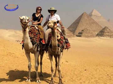 Touristes à dos de chameau devant les pyramides